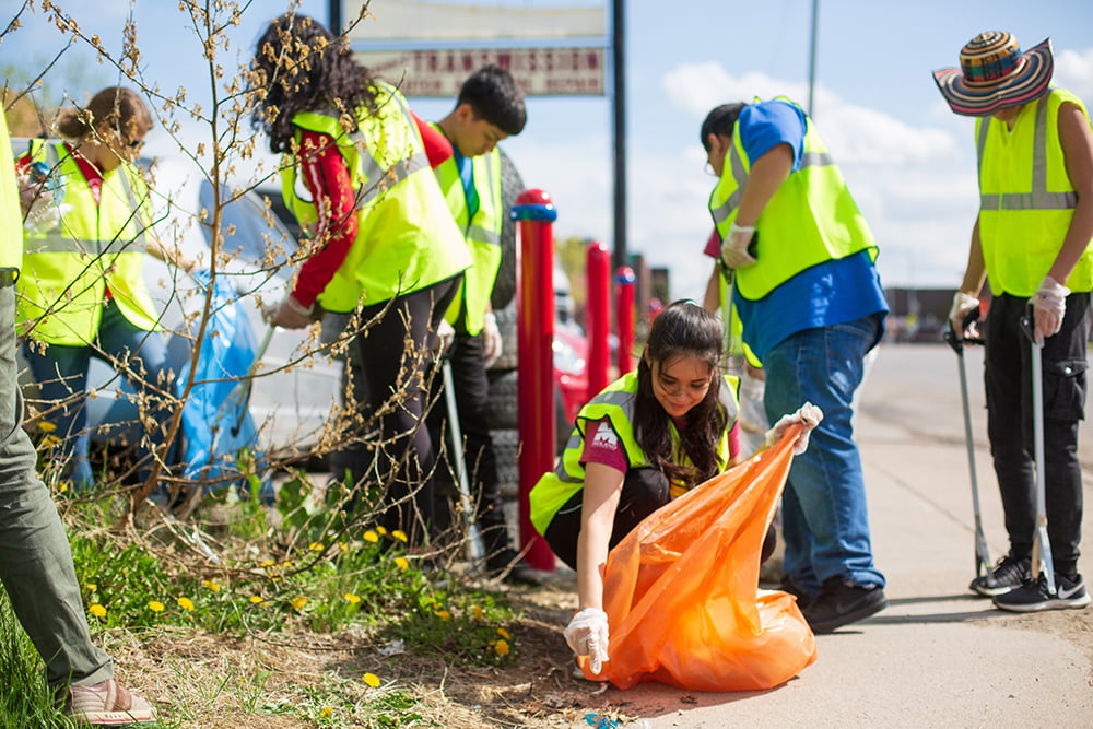 Community members cleaning roadside trash with gloves and garbage bags